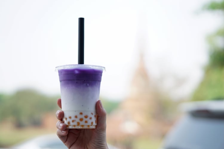 A hand holding a glass of iced taro latte with boba on blurred background