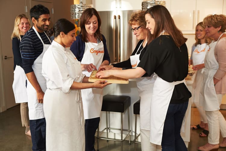 A chef handing out food to people (all wearing Cozymeal aprons) during a cooking class