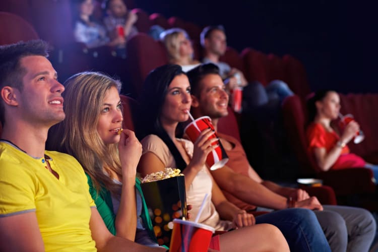 People sitting in a cinema watching a movie with snacks and drinks.