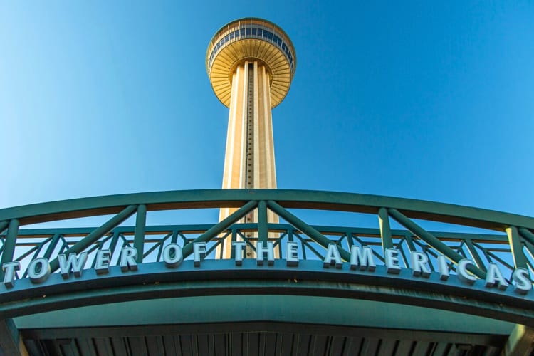 A low angle shot of the Tower of the Americas with a sign that says: 