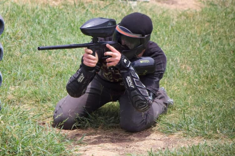 One person on their knees, pointing a paintball gun forward, at XFactor Paintball Park