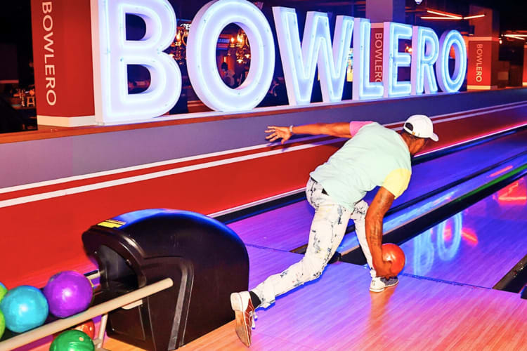 A person who's about to release a red ball while bowling at Bowlero