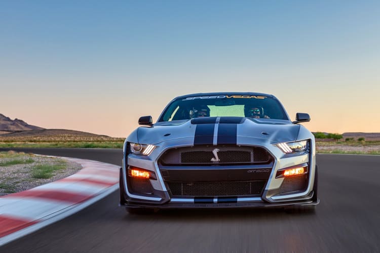 Two people in a Ford Mustang Shelby driving on a road