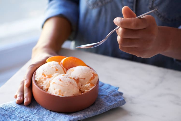 A hand holding a bowl of ice cream with another hand holding a spoon