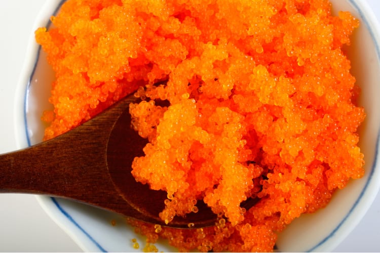 Organge tobiko on a wooden spoon in a ceramic dish