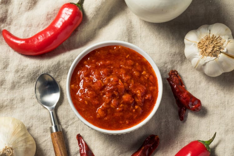 Red harissa paste on a table surrounded by ingredients such as garlic and peppers.