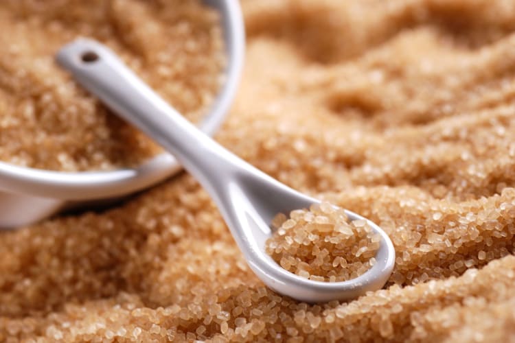 Brown sugar spilling out of a white bowl in a small spoon