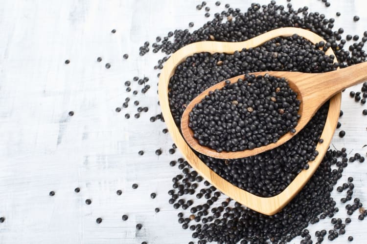 A wooden spoon of black beluga lentils in a heart-shaped bowl