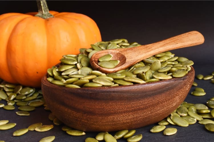 A bowl of pepitas next to a pumpkin