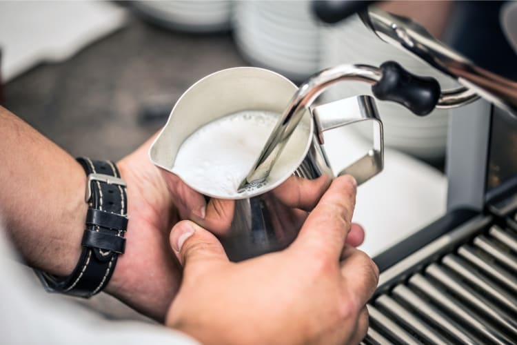 A barista froths up milk for a cortado coffee