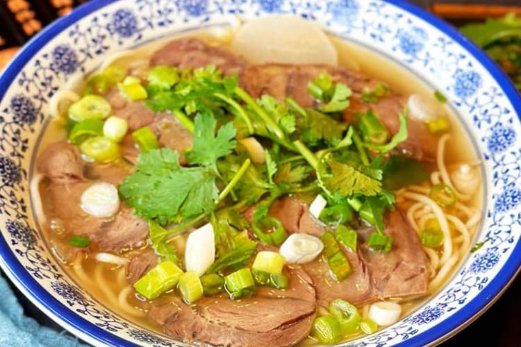 beef noodles soup with seasoned broth and scallions served in a white and blue plate