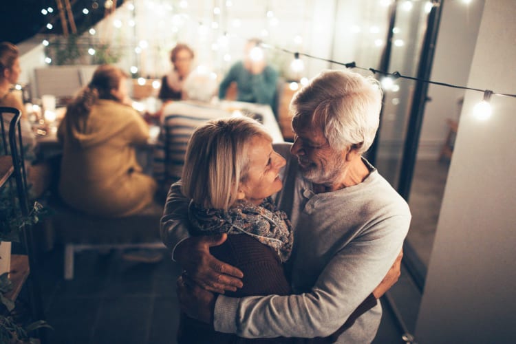 a senior couple embracing at a party and smiling at each other