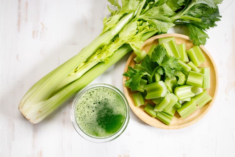 Whole and chopped celery with a glass of celery juice.