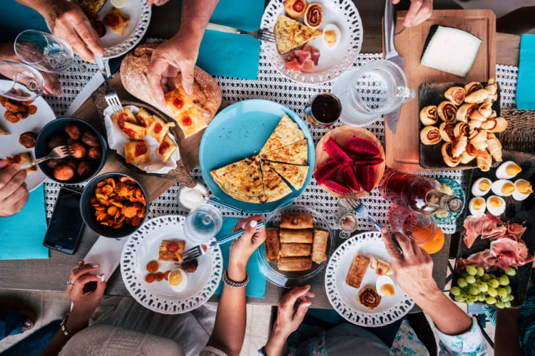 A table of people fill their plates with buffet food items including quesadilla, cold cuts and eggs.