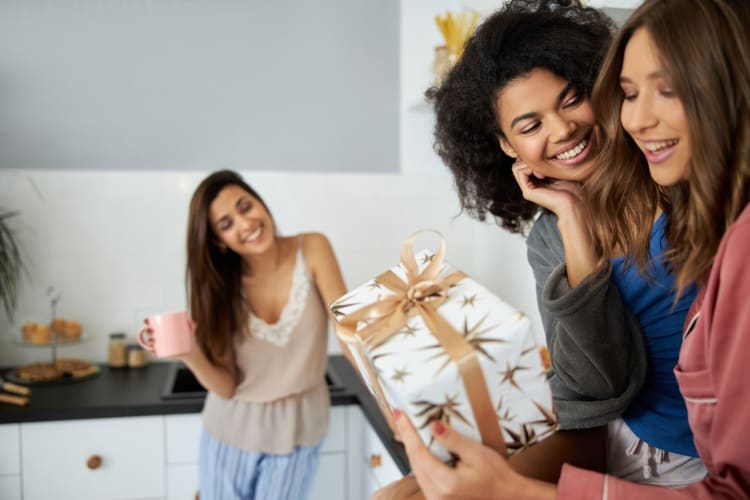 Woman giving her girlfriend a gift while another woman looks on smiling