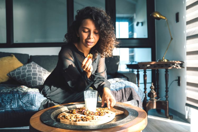 woman mindfully enjoying dates and nuts on her sofa in the evening