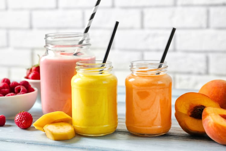 Three colorful fruit smoothies in glass jars next to fruit