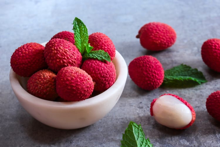 Fresh lychee in a bowl next to more lychee