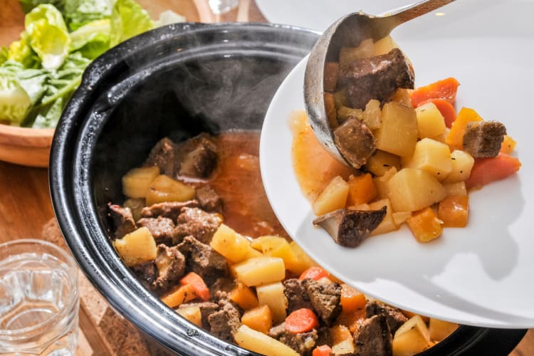 a slow cooker full of steaming stew being dished out onto a plate