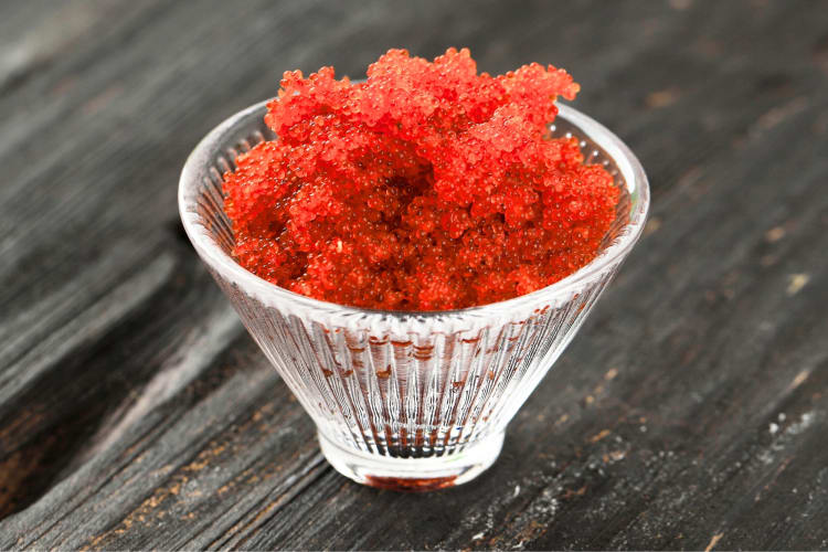 Red tobiko in a glass dish on a wooden surface