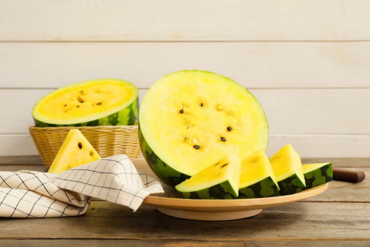 Cut pieces of yellow watermelon on a plate on a wooden table