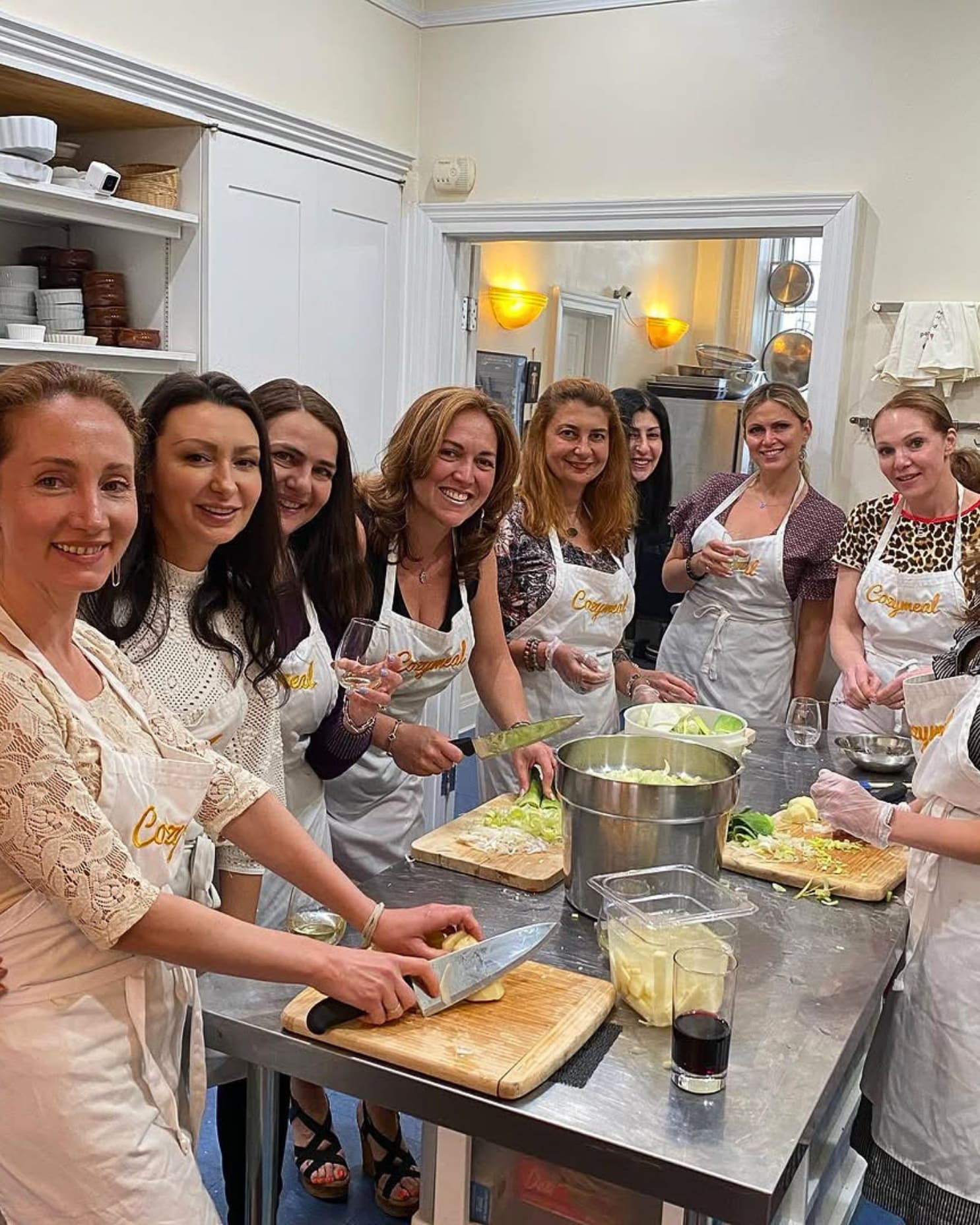 A group of women wearing Cozymeal aprons prepares vegetables together around a kitchen worktable in a team building activity in Los Angeles.