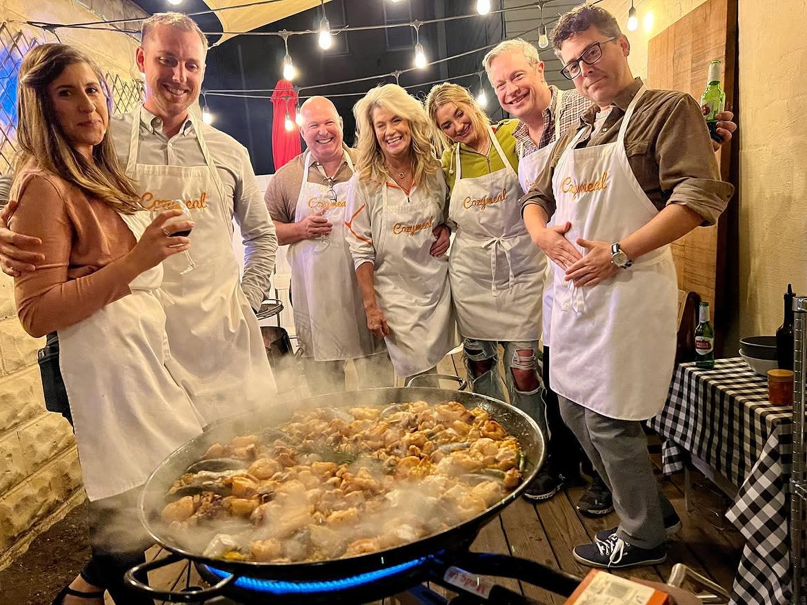 Nine participants wearing Cozymeal aprons stand behind trays of handmade pasta and pasta drying racks in a pasta-making class in NYC.