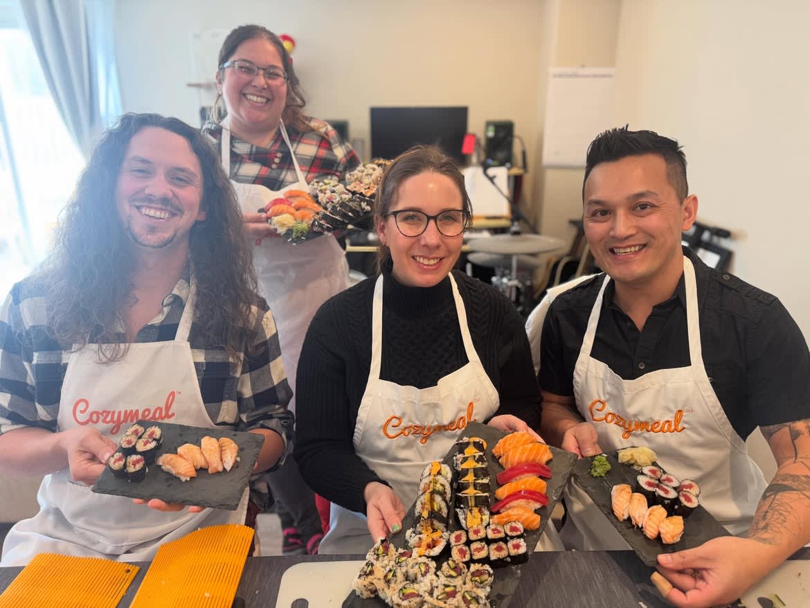 Four participants wearing Cozymeal aprons display platters of sushi rolls and nigiri in a team building activity in San Francisco.