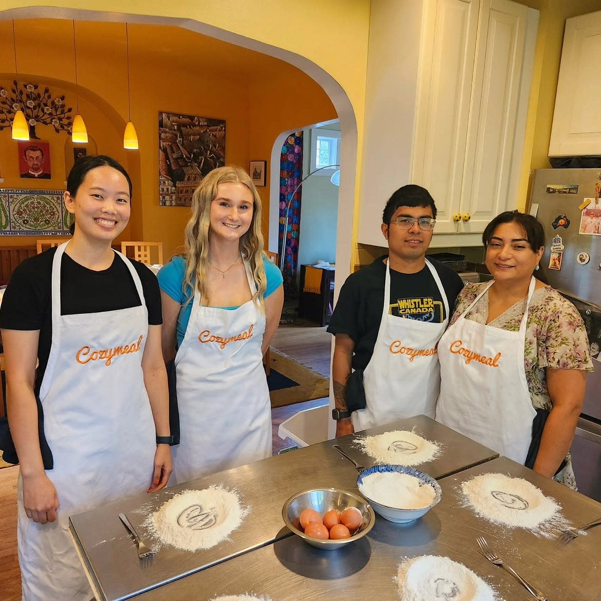 Four participants wearing Cozymeal aprons stand behind a kitchen table set with flour and eggs for a pasta making class in Los Angeles.