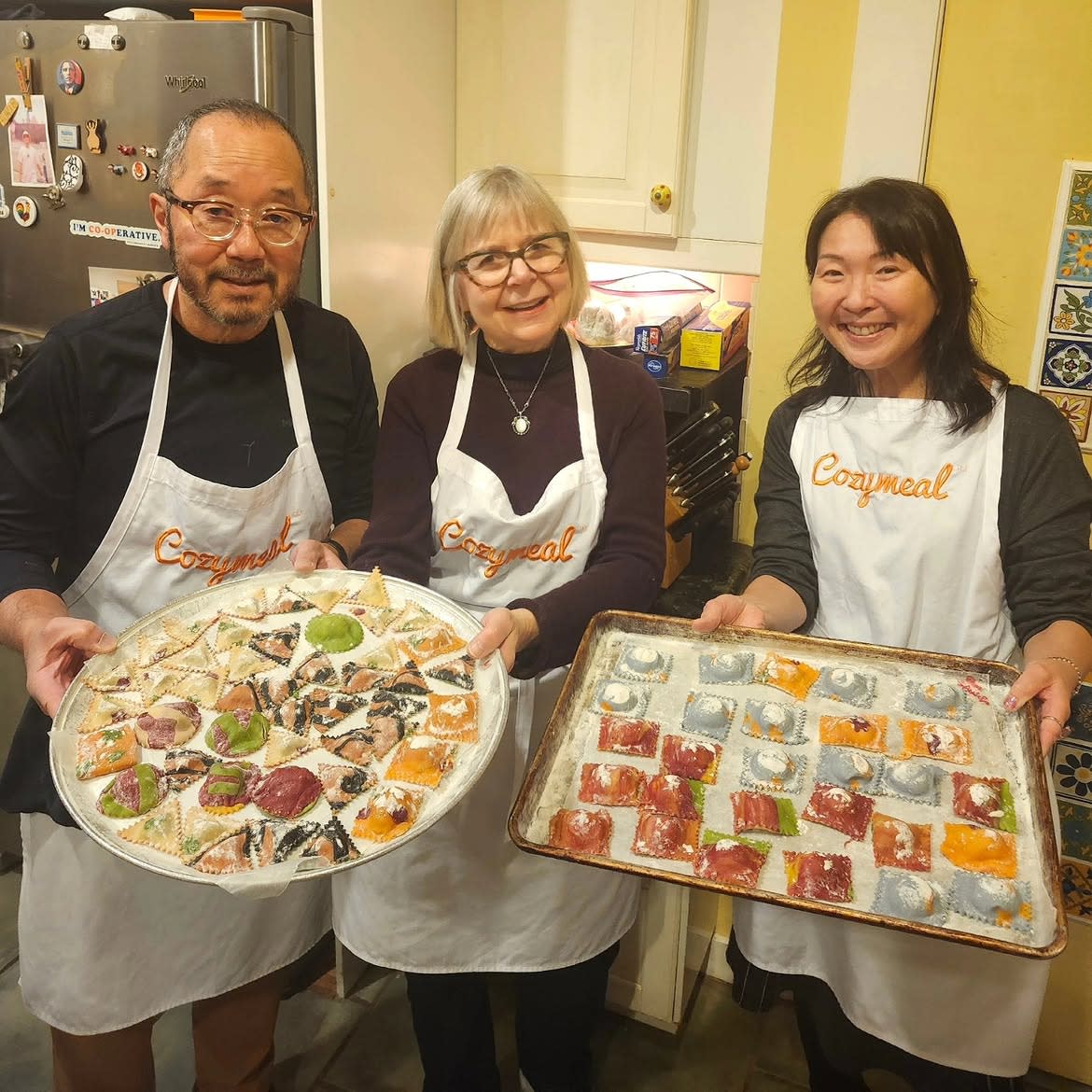 Three participants wearing Cozymeal aprons display trays of colorful handmade ravioli in a kitchen during a cooking class in Los Angeles.