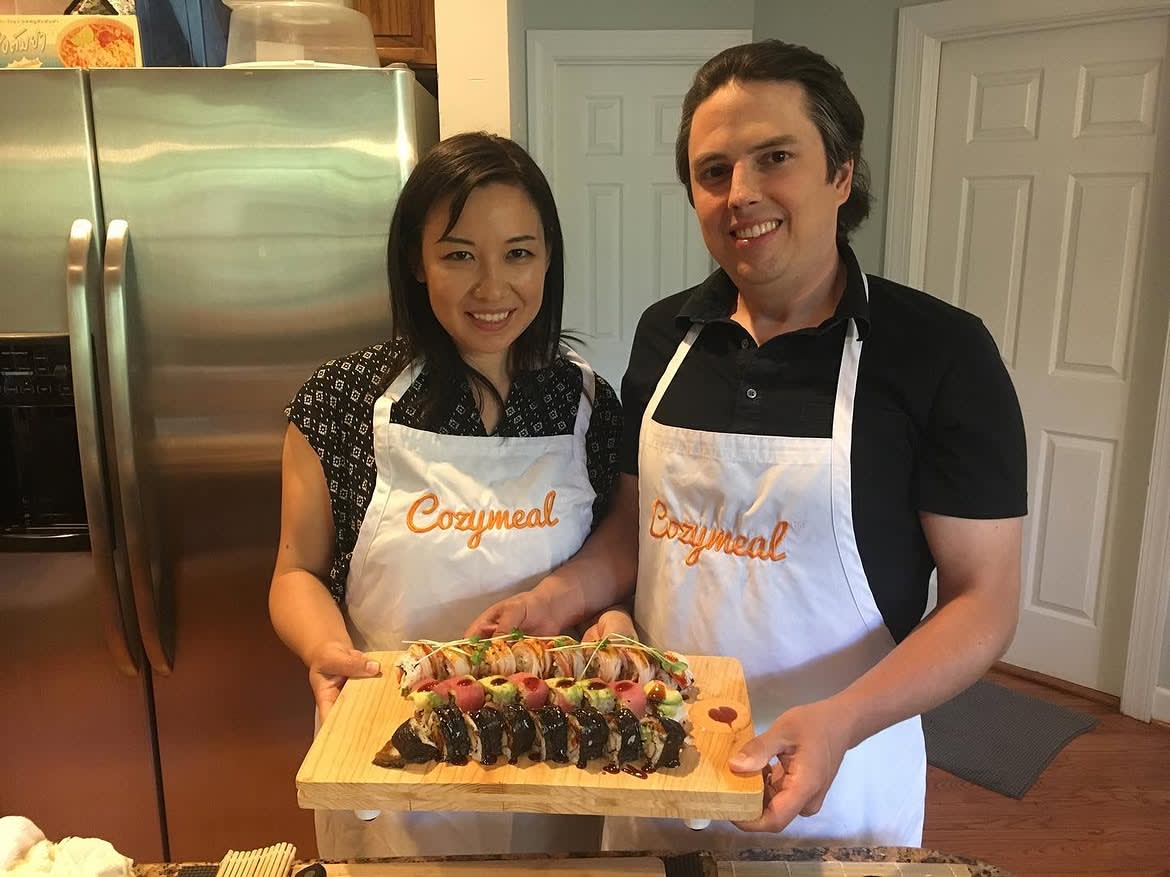 Two participants holding a wooden board of sushi rolls at a cooking class in NYC.