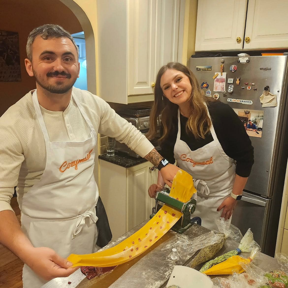 Two participants rolling fresh pasta dough through a pasta machine at a cooking class in NYC.