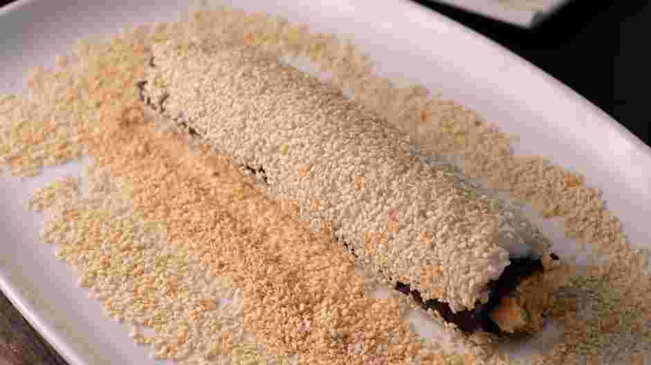 Salmon Skin Roll Recipe: Roll the salmon skin roll in toasted sesame seeds to coat the outside.