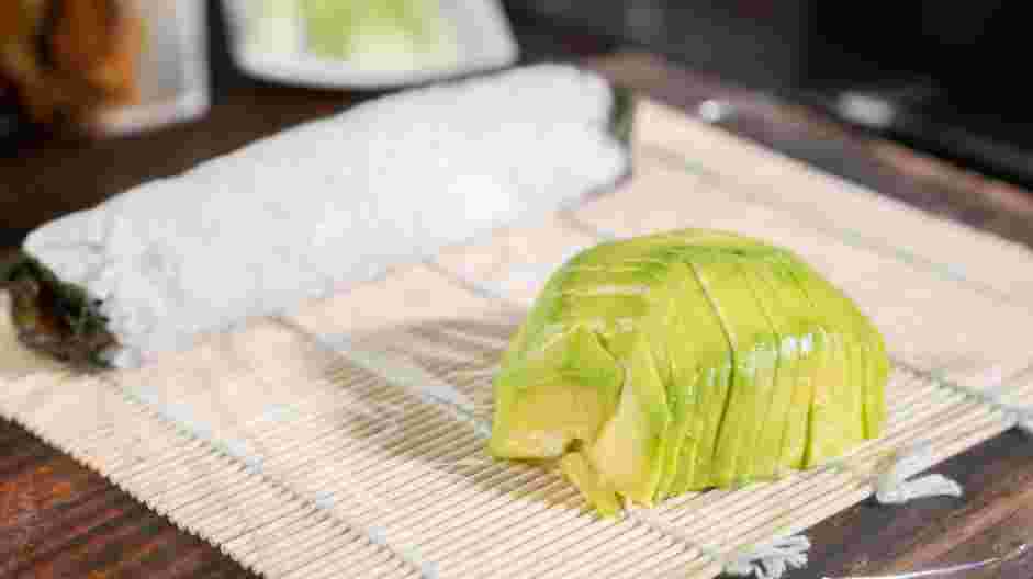 Easy Caterpillar Roll Recipe: Place the sliced avocado on one side of the wax paper or plastic wrap, opposite the sushi roll.