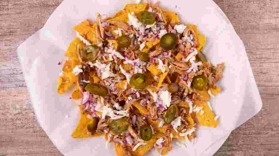 Pulled Pork Nachos Recipe: Evenly spread half of the chopped red onion and pickled jalapeños over the cheese.