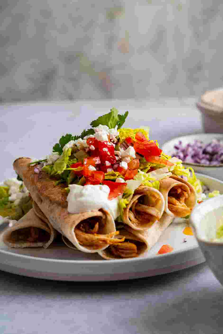 Chicken Flautas Recipe: Serve topped with shredded lettuce, sour cream, chopped red onions, chopped tomatoes, cojita cheese and fresh cilantro.