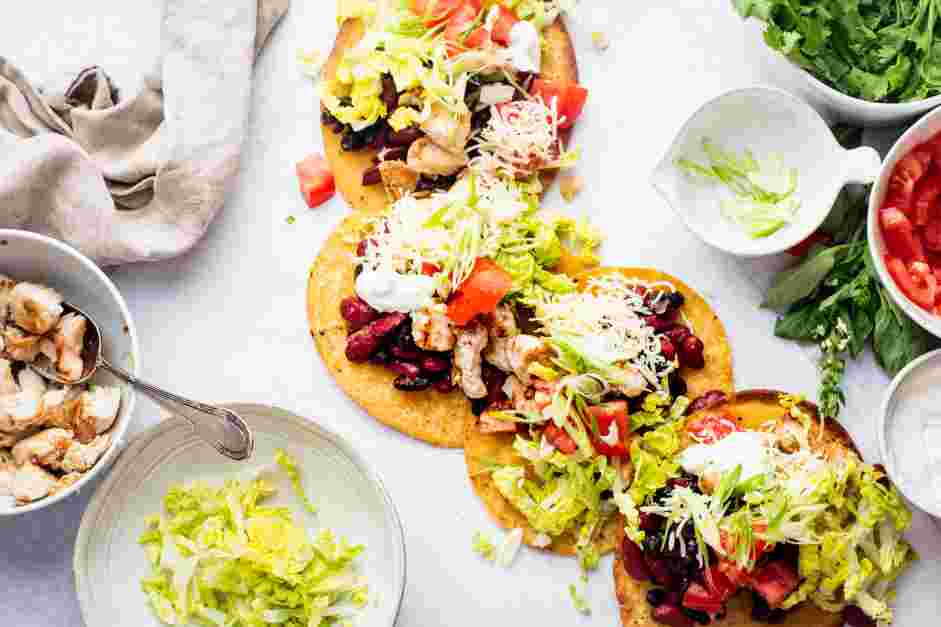 Chicken Tostadas Recipe: Sprinkle on the cheddar cheese, then the chopped salad greens, chopped Roma tomatoes and avocado slices.