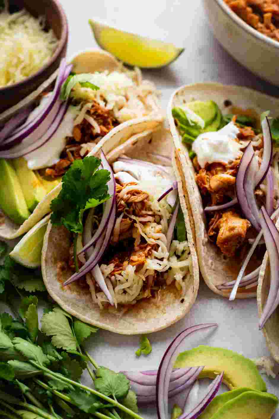 Instant Pot Chicken Tacos Recipe: Serve the Instant Pot chicken tacos with tortillas, sliced avocados, shredded cheese, sour cream, cilantro and lime wedges.