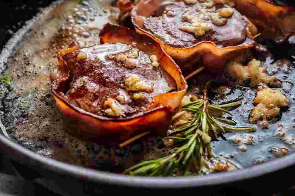 Bacon Wrapped Filet Mignon Recipe: Flip the steaks and add the butter, smashed garlic cloves and rosemary sprigs to the skillet.