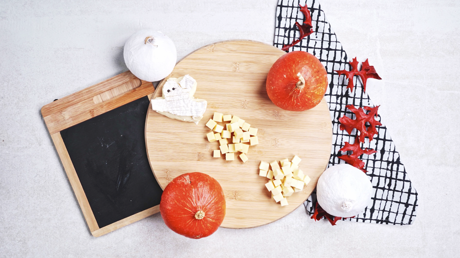 Halloween Charcuterie Board Recipe: Place the ghost shaped brie, cubed sharp cheddar cheese and Gouda cheese on the board, arranging each cheese on the upper left, center and bottom right.