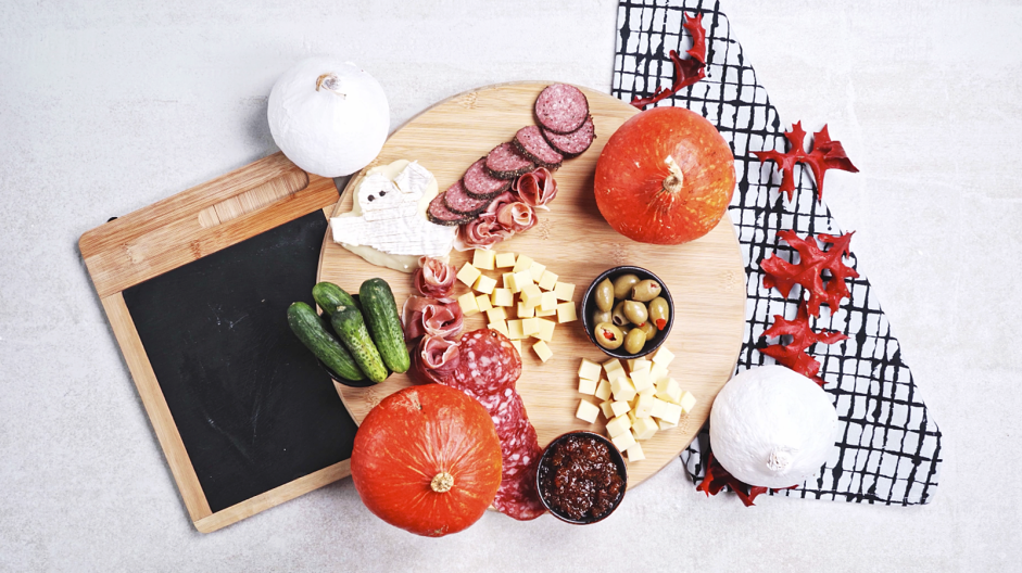 Halloween Charcuterie Board Recipe: Place three small bowls on opposite ends of the board and fill one with olives, one with fig jam and the other with cornichons (or pickles).