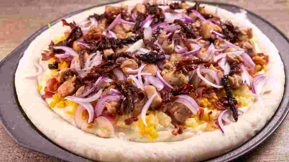 Chicken Bacon Ranch Pizza Recipe: Spread the ranch sauce, mozzarella, gouda, chopped bacon, cooked chicken thighs, red onions and sundried tomatoes on the partially baked pizza dough.