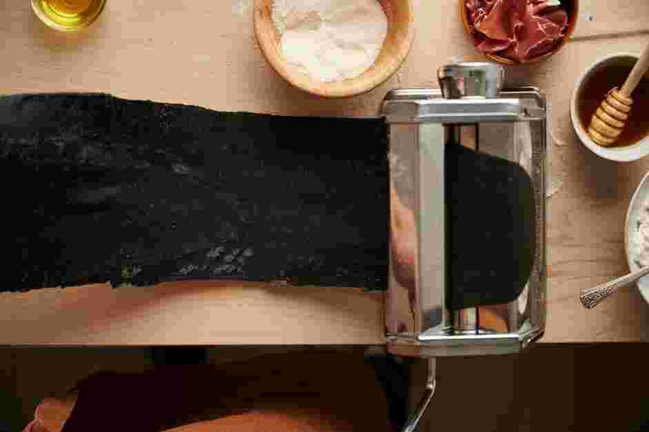 Squid Ink Pasta with Crispy Prosciutto and Truffle Honey Recipe: Fold again and reduce the thickness of the pasta roller by one notch, and continue reducing the number as you roll and fold 2-3 times.