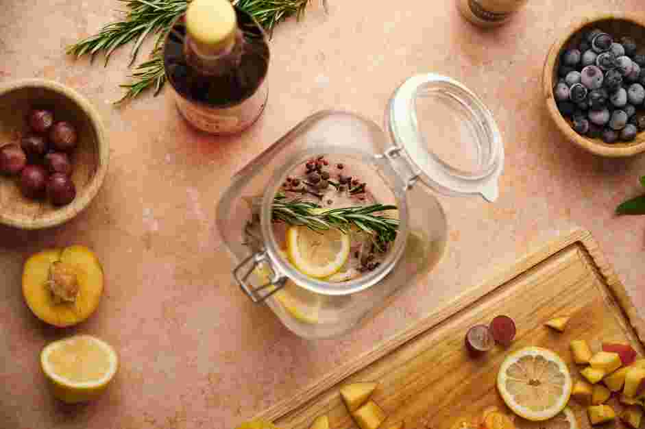 Moscato Sangria Recipe: In a large clear glass pitcher or punch bowl, place the juniper berries, pink peppercorns, whole cloves, lemon slices and one sprig of rosemary.