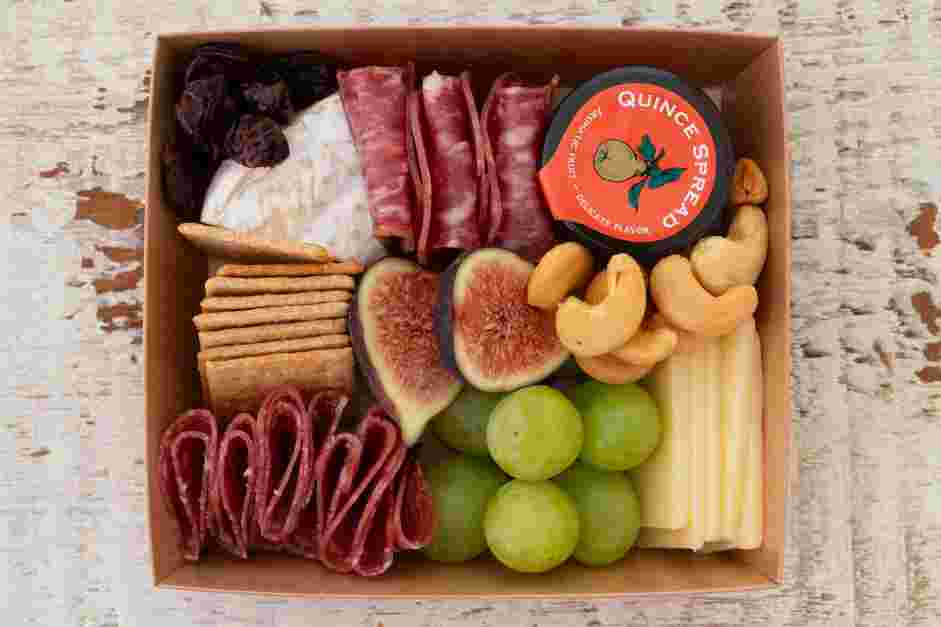 Mini Charcuterie Boxes Recipe: Add ingredients into individual boxes, starting with the meats, cheeses and jam pot.