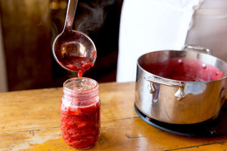 ladeling homemade strawberry jam into a jar