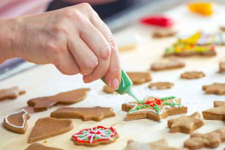 person applying green decoration to gingerbread cookie