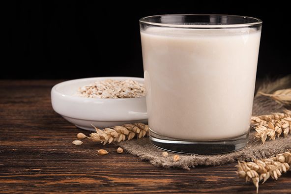 Im Vordergrund ein Glass voll Milch, im Hintergrund eine Weizenähre und eine Müslischüssel