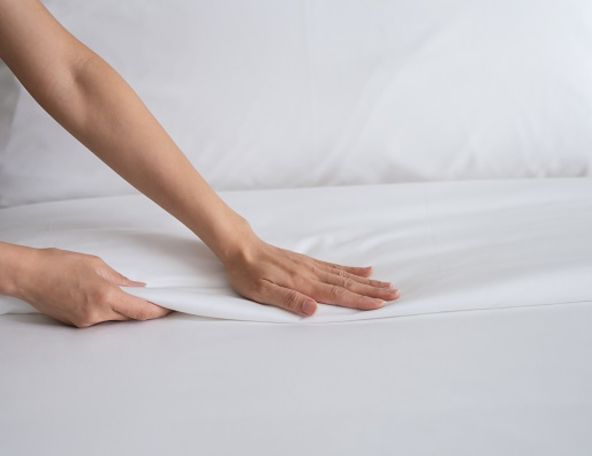 Eine Frau streicht die Bettdecke eines Hotelsbetts glatt. | B&B HOTELS