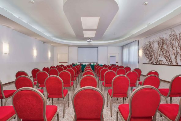 Sala meeting a Conegliano con muri bianchi e sedie rosse